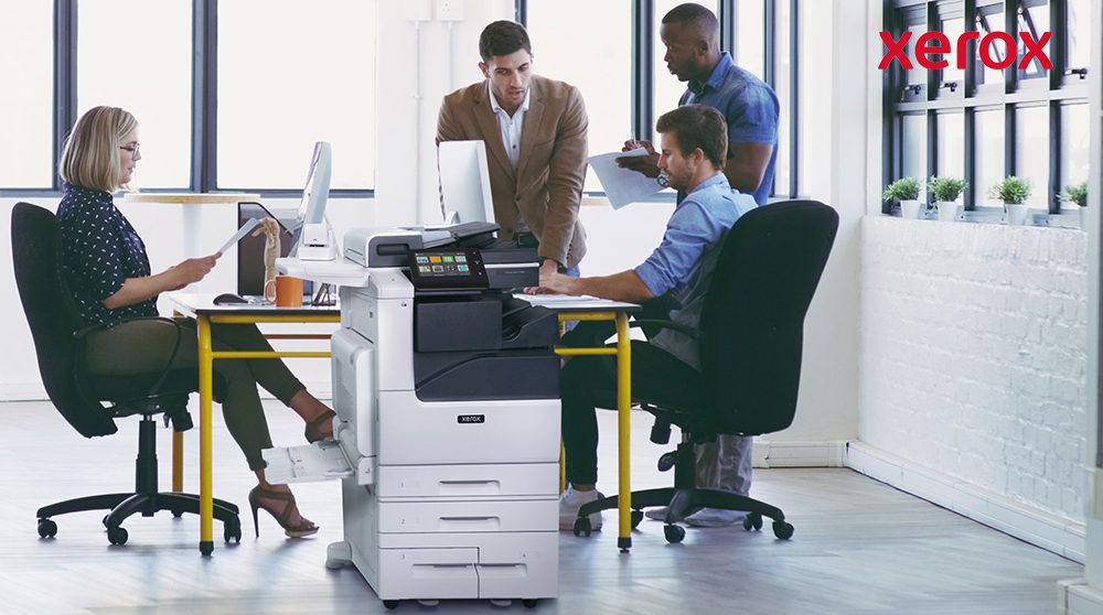 Employés de bureau collaborant à proximité d'une imprimante Xerox. Employés de bureau collaborant à proximité d'une imprimante Xerox.