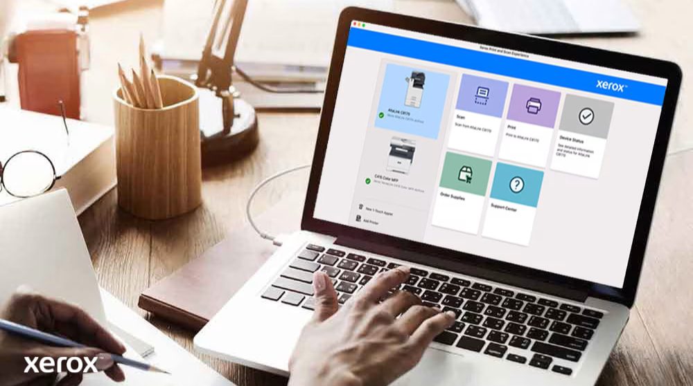 Expérience d'impression et de numérisation Xerox® : contrôle intuitif Les mains d'une personne sont posées sur un clavier d'ordinateur portable et l'écran affiche l'interface Xerox Print and Scan Experience avec des options telles que Numériser, Imprimer, État de l'appareil, Commander des fournitures et Centre d'assistance, indiquant un contrôle convivial.