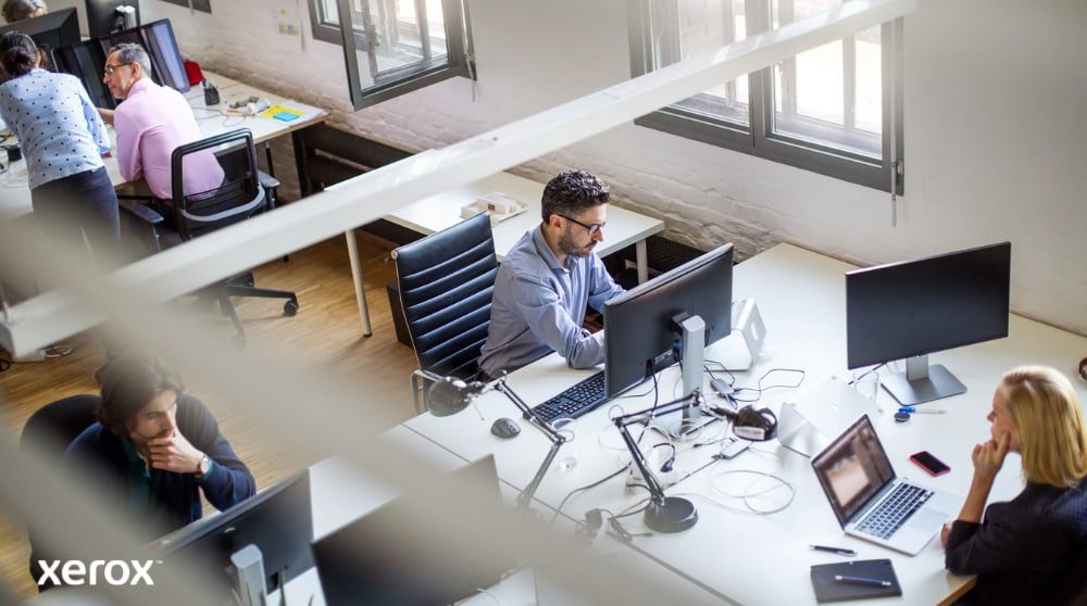 Expérience d'impression et de numérisation Xerox® : Optimiser la productivité du bureau Vue aérienne d'un espace de bureau ouvert où plusieurs personnes travaillent à leur bureau, devant un ordinateur. La scène évoque un environnement de travail productif et collaboratif.