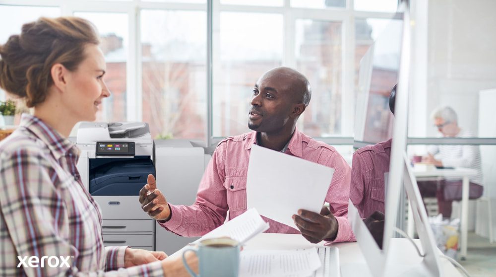 Xerox® Workplace Cloud et Suite : gestion centralisée du parc Une personne examine des données sur l'écran d'un ordinateur portable, avec une superposition numérique de diverses icônes d'appareils (imprimantes, appareils mobiles) et de lignes connectées, symbolisant la gestion centralisée de la flotte pour Xerox Workplace Solutions.